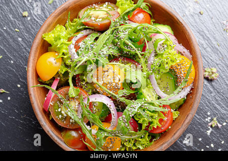 Vista superiore in insalata di verdure di lattuga, pomodori ciliegini, rafano, cetriolo, cipolla e basilico sul vassoio di ardesia Foto Stock