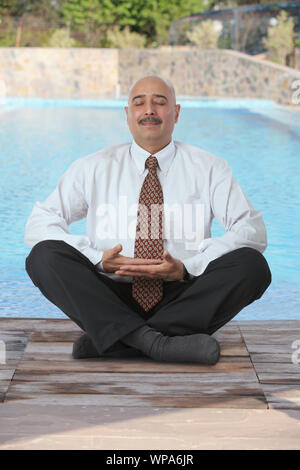 Uomo d'affari che pratica yoga a bordo piscina Foto Stock