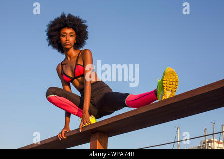 Felice giovane donna africana di stretching e riscaldamento prima di un allenamento all'aperto. con un bel cielo azzurro sullo sfondo Foto Stock