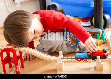 Bambino caucasico, 3-4 anni, all'interno. Il livello del pavimento vista del giovane ragazzo giocando con Thomas Tank Engine train set. Spingendo il treno lungo la via. Foto Stock