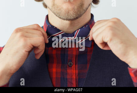 Giovane uomo attraente con barba che indossa bowtie con le mani sulla foto correggendo il suo bowtie, hippster stile. Concetto di abbigliamento per il lavoro, lo stile di vita e le bowtie. Foto Stock