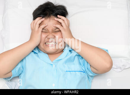 Malati fat boy che soffrono di mal di testa sul letto, vista dall'alto ed emicrania o il concetto di stress Foto Stock