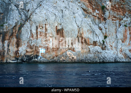 Isola di Symi, Grecia, Agosto 2019. Vista la bandiera greca dipinta sulla scogliera Foto Stock