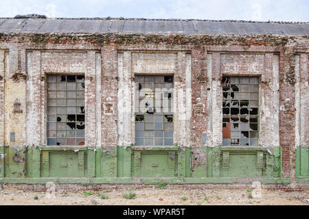 Outdoor soleggiata vista esterna di vetro danneggiato windows e un muro di mattoni facciata della ex abbandonare edificio industriale. Foto Stock