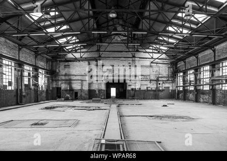 Tono di BW,vista interna del vuoto piano aperto di abbandonare la ex fabbrica di officina con danni di elementi di costruzione, a parete, windows e soffitti con nessuno. Foto Stock