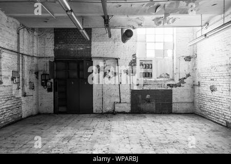 BW tono, vista interna del vuoto abbandonare la sala con graffi danneggiato un muro di mattoni e il soffitto e rottura di vetri di finestra sporca, pavimento in piastrelle e con nessuno. Foto Stock