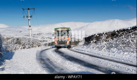 Alimentazione animale azienda carro che viaggiano lungo una coperta di neve strada rurale, Cumbria, Regno Unito. Foto Stock