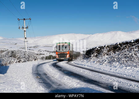 Alimentazione animale azienda carro che viaggiano lungo una coperta di neve strada rurale, Cumbria, Regno Unito. Foto Stock