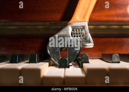 In prossimità di una chiave regolabile holding e premendo un tasto di pianoforte. La sintonizzazione, fat finger nei mercati finanziari, dissonanza in musica concetti. Foto Stock