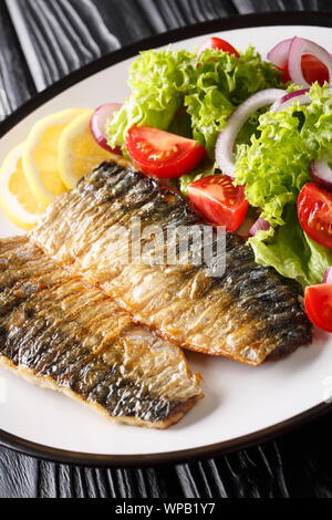 Grigliata di filetti di sgombro con insalata fresca e limone close-up su una piastra sul piano verticale. Foto Stock