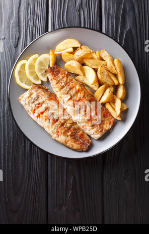 Servizio di grigliate di filetti di sgombro con spicchi di patate e limone closeup su una piastra sul tavolo. Verticale in alto vista da sopra Foto Stock