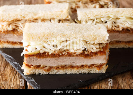 Giapponese fast food katsu sando panini con salsa tonkatsu e cavolo closeup su una scheda di ardesia su una tavola di legno orizzontale. Foto Stock