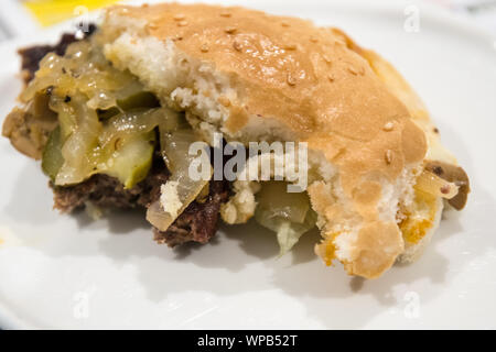 Mezza mangiato semi di sesamo coperto burger bun con juicy patty e gustose cipolle e cetrioli Foto Stock