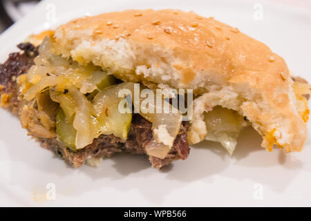 Mezza mangiato semi di sesamo coperto burger bun con juicy patty e gustose cipolle e cetrioli Foto Stock