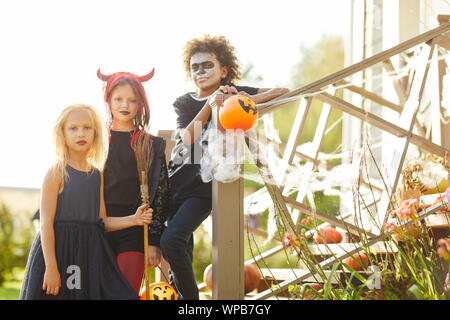 Multi-etnico gruppo di bambini trucco o trattare su Halloween, bambini guardando la telecamera mentre sta in piedi sulle scale di casa decorata, spazio di copia Foto Stock