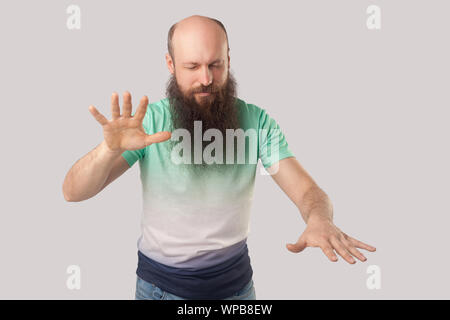 La cecità. Ritratto di mezza età uomo calvo con la barba in luce verde t-shirt in piedi con gli occhi chiusi e cercando di toccare o trovare qualcosa. i Foto Stock