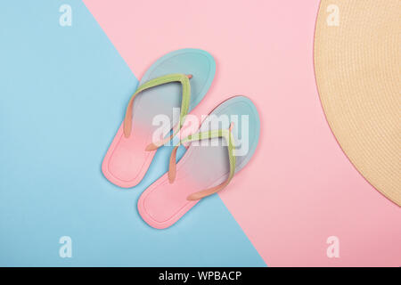 Elegante spiaggia flip-flop e cappello per il sole in rosa e blu sullo sfondo color pastello, vista dall'alto. Estate concetto minimalista con copia spazio. Foto Stock