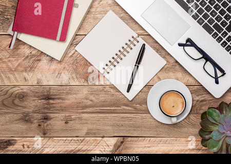 In legno rustico desk top view con notebook, penna, laptop e la tazza di caffè. Area di lavoro con copia spazio. Il lavoro di ufficio, di studio o di scrittura di concetti. Foto Stock