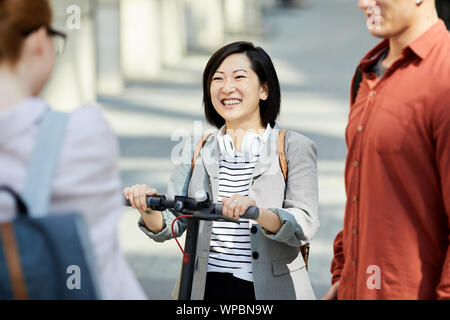 Gruppo di contemporanea giovani chiacchierando in una strada di città, concentrarsi sulla donna asiatica sorridente felicemente, spazio di copia Foto Stock