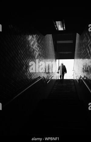 MATSUYAMA, Giappone - Agosto 03, 2019: una scala di grigi colpo verticale di una persona salire le scale con un corrimano su un muro di mattoni Foto Stock