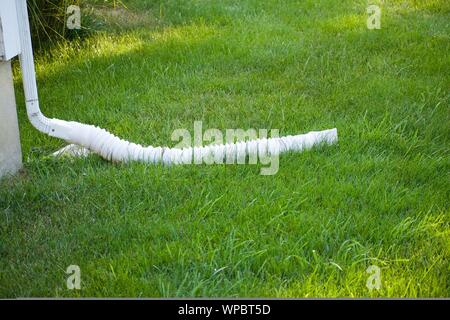 Verso il basso il tubo di lancio dalla casa il drenaggio di acqua in un cortile erboso lontano da casa. L'acqua piovana, tubo di lancio di canaletta di scarico verso il basso Foto Stock