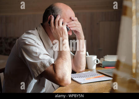 Senior uomo sensazione sconvolto avente conversazione telefonica premuta da audizione cattive notizie seduti a casa Foto Stock