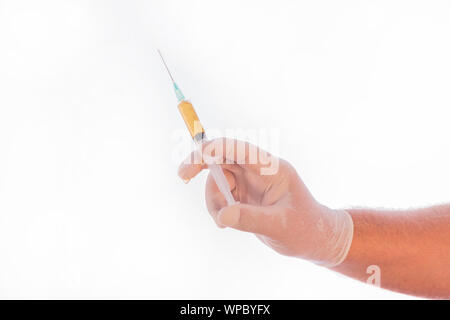 Dettaglio foto di una siringa piena di medicina tenuto dalla mano di un medico coperto da un guanto di medici su uno sfondo bianco. Spazio per la scrittura. Foto Stock