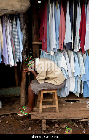 KIBERA, KENYA-dicembre 6, 2010: Unidentified negoziante appoggia la testa durante il tentativo di vendere camicie di Kibera, Africas più grande baraccopoli urbane. Foto Stock