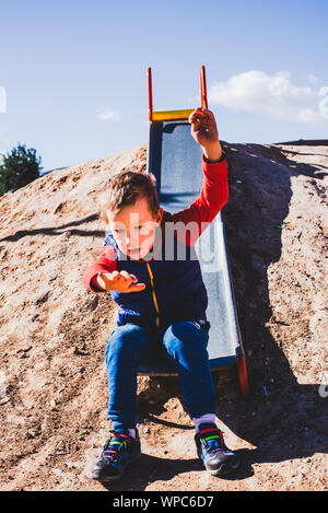 Bambino lo scorrimento verso il basso una vecchia diapositiva di metallo in un campo. Foto Stock