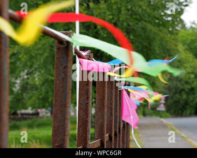 Multi-colore bunting tradizionali fiamme fissato alla strada arrugginito ringhiere svolazzamento nella brezza in un villaggio in Cumbria,l'Inghilterra,UK Foto Stock