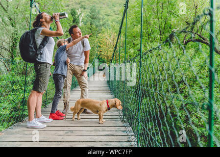 Famiglia con piccolo cane giallo in piedi su una tavola di legno ponte di sospensione e di appoggio Foto Stock