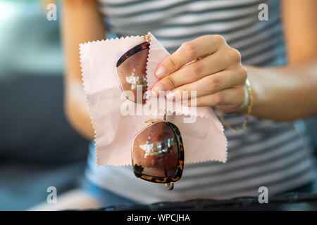 Donna di pulizia delle mani i suoi occhiali da sole con un panno in microfibra di pulizia, wipping occhiali da sole Foto Stock