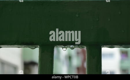 Primo piano trasparente di gocce di pioggia sulla balaustra verde sul giorno di pioggia, il fuoco selettivo Foto Stock