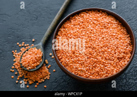 Rosso Secco lenticchie in un recipiente su sfondo nero. Sana vegetariano vegano alimenti ricchi di proteine Foto Stock