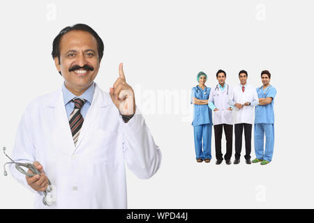 Medico maschile che punta verso l'alto con la squadra in background Foto Stock