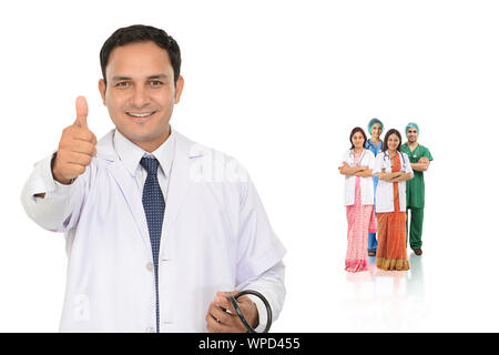 Fidato medico maschile mostrando pollici fino segno con la squadra in background Foto Stock