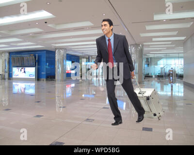 Uomo d'affari che tira la valigia al terminal dell'aeroporto Foto Stock