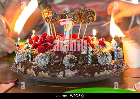 Impostazione fuoco ad un candele su una festa di compleanno per bambini torta, mani con la masterizzazione di corrispondenze in bokeh di fondo. Foto Stock