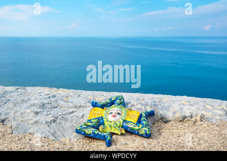 Tradizionale souvenir siciliano, Trinacria in ceramica su una pietra vicino al mare. Cefalu, Sicilia, Italia Foto Stock