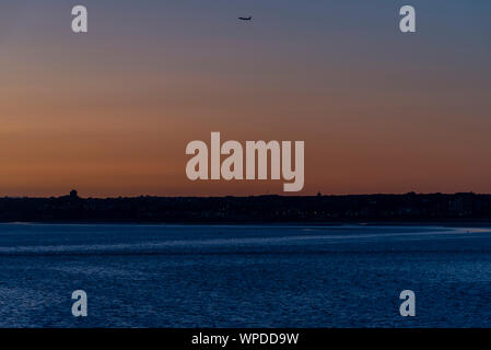 Un aereo di linea in partenza dall'aeroporto Southend di Londra, Essex, Regno Unito, al tramonto. Viaggi aerei. Volare verso il tramonto. Oscuro. Sopra Southend Town Foto Stock