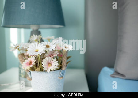 In prossimità dei fiori e la lampada sul tavolo con sunray in camera da letto. Cuscino grigio sul copriletto blu. Foto Stock