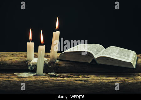 Bellissima Bibbia aperta e bruciate candele su una vecchia quercia tavolo in legno e uno sfondo scuro. Foto Stock