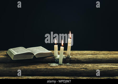 Bellissima Bibbia aperta e bruciate candele su una vecchia quercia tavolo in legno e uno sfondo scuro. Foto Stock