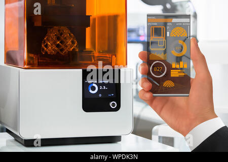 Mano con futuristico smartphone trasparente. Domanda di controllo stampante 3D in laboratorio. Foto Stock