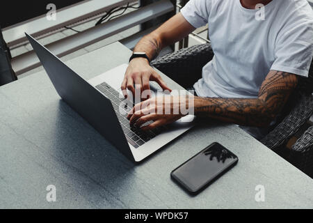 Bel ragazzo con tatuato mani vestito camicia bianca lavorando su laptop, maschio a digitare il testo sulla tastiera del notebook. Il freelance che lavorano su nuove startup proje Foto Stock
