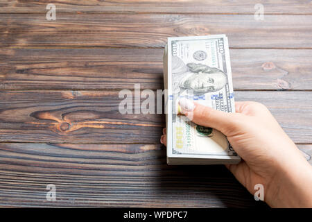 Femmina lato tenendo un fascio di un centinaio di dollari di banconote su sfondo di legno. Stipendi e salari con il concetto di spazio di copia. Foto Stock