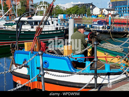 Senior uomo seduto sulla colorata barca ormeggiata in porto turistico, Hull, East Yorkshire, Inghilterra, Regno Unito Foto Stock