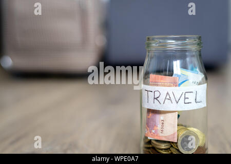 Il vasetto di vetro sul pavimento marcato in viaggio la messa a fuoco e una borsa da viaggio in background al di fuori della messa a fuoco. Pavimento in legno. Foto Stock