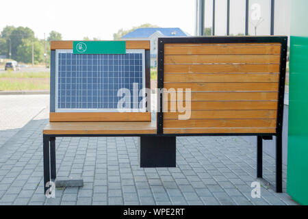 Colpo all'aperto della panca di legno nel parco con energia solare pannello installato, cavo USB collegato allo smartphone Foto Stock