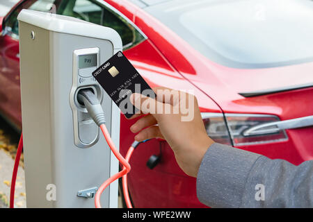 Un uomo paga per la ricarica di un auto elettrica. Foto Stock